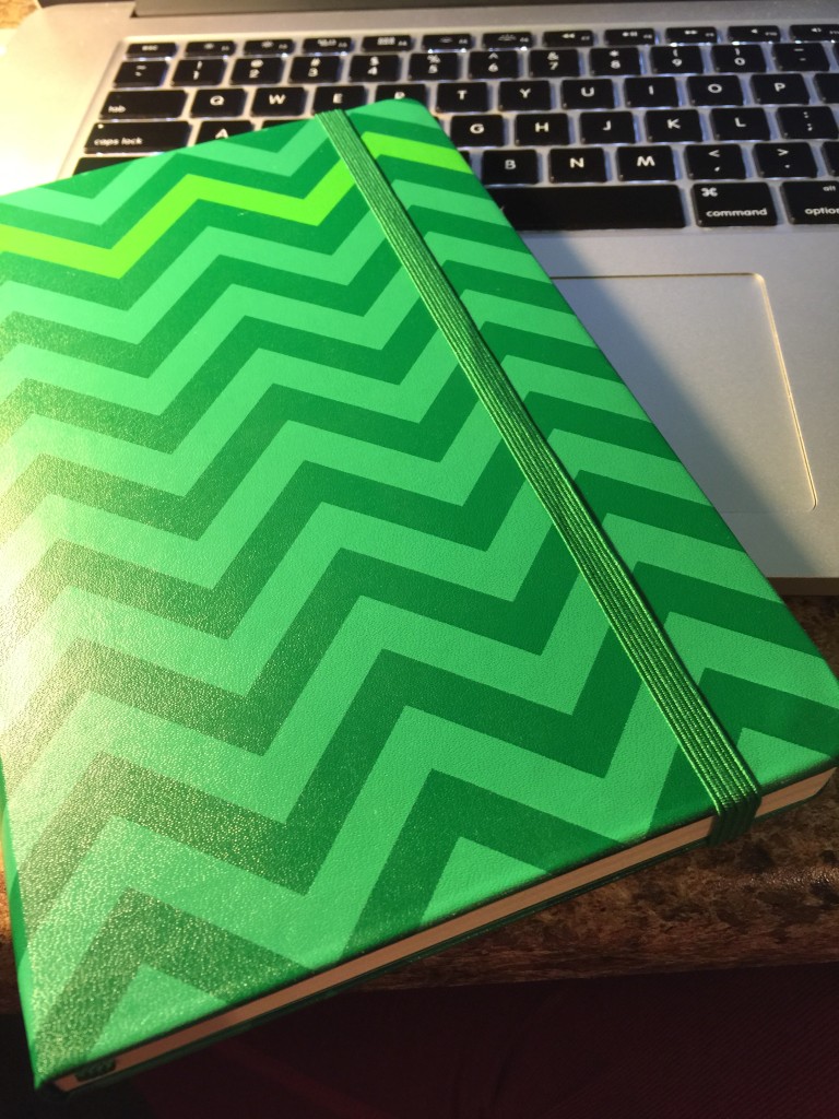 A green chevron-patterned notebook with elastic band resting on a laptop keyboard, close up